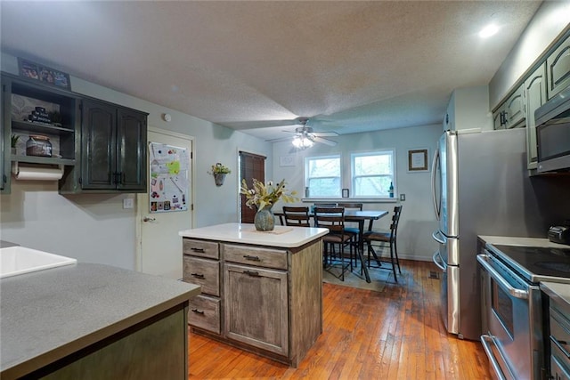 kitchen with a kitchen island, stainless steel appliances, a ceiling fan, and hardwood / wood-style floors