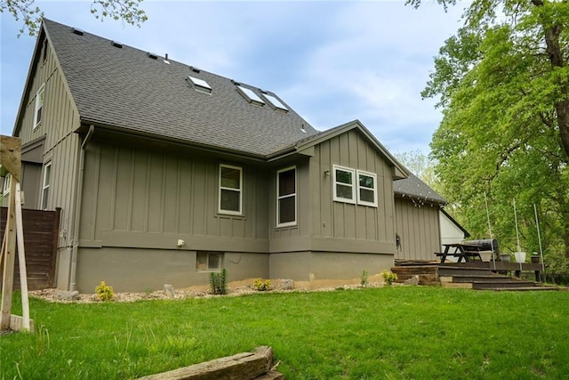 rear view of house featuring board and batten siding, a yard, and a shingled roof