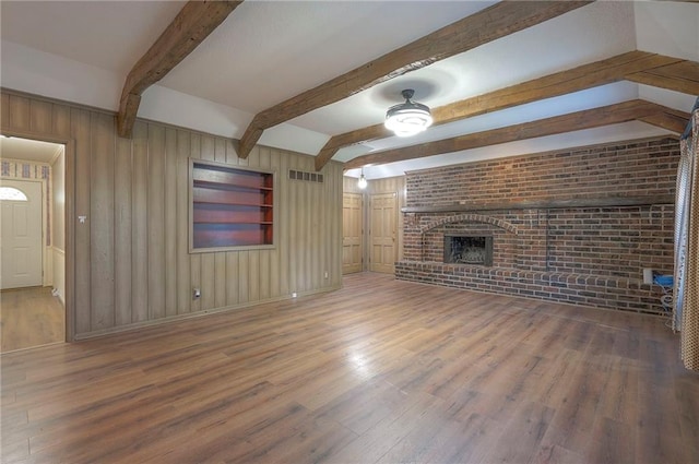 3913 Stonewall Ave, Independence, MO 64055 - unfurnished living room with brick wall, visible vents, a fireplace, wood finished floors, and beamed ceiling