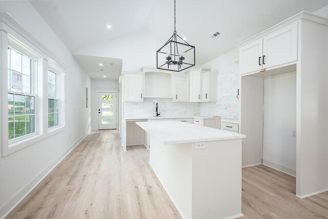 kitchen featuring a center island, a chandelier, tasteful backsplash, light wood-style flooring, and hanging light fixtures