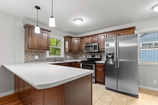 kitchen with stainless steel appliances, a sink, a peninsula, light countertops, and decorative backsplash