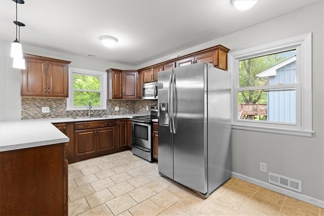 kitchen with stainless steel appliances, a sink, decorative backsplash, light countertops, and pendant lighting