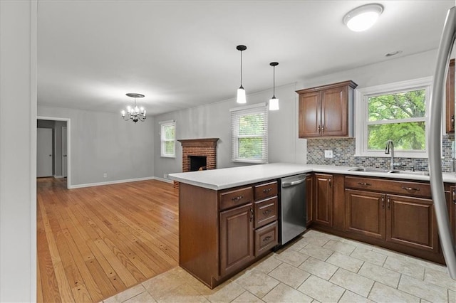 kitchen featuring stainless steel dishwasher, a sink, a peninsula, light countertops, and a chandelier
