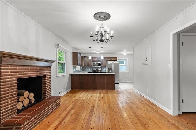 kitchen featuring appliances with stainless steel finishes, a chandelier, a peninsula, light wood finished floors, and baseboards