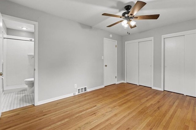 unfurnished bedroom featuring two closets, light wood-style flooring, ensuite bathroom, baseboards, and ceiling fan