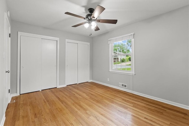 unfurnished bedroom with multiple closets, baseboards, light wood-style flooring, and a ceiling fan