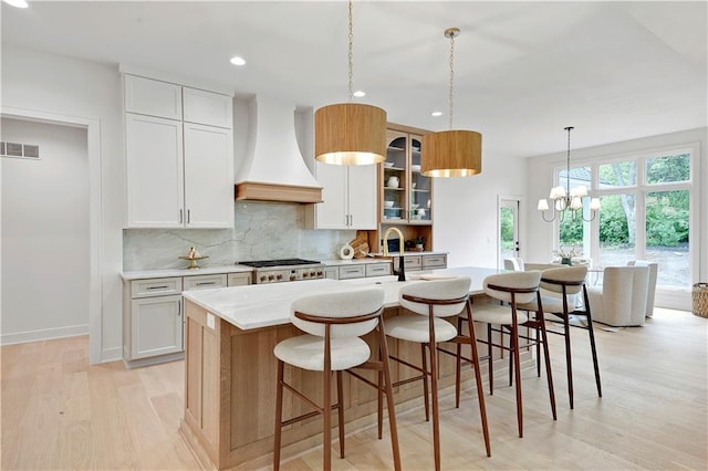 17045 S Highland Ridge Dr, Loch Lloyd, MO 64012 - kitchen with custom exhaust hood, light wood-style flooring, an island with sink, backsplash, and a chandelier