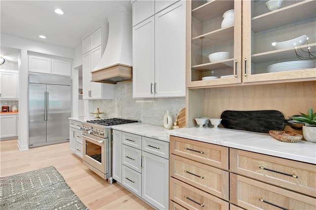 17045 S Highland Ridge Dr, Loch Lloyd, MO 64012 - kitchen featuring premium appliances, custom range hood, light wood-style flooring, backsplash, and glass insert cabinets