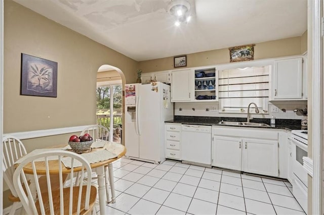 kitchen featuring dark countertops, a sink, white appliances, arched walkways, and tasteful backsplash