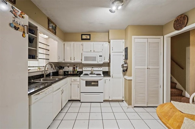 kitchen with a sink, dark countertops, white cabinets, and white appliances