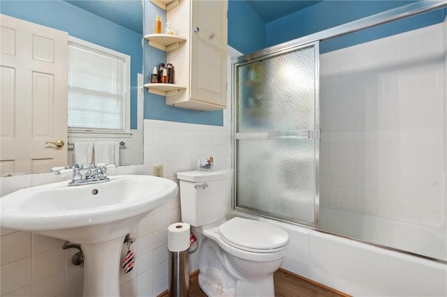 2106 Kasold Dr, Lawrence, KS 66047 - full bath featuring tile walls, wainscoting, wood finished floors, bath / shower combo with glass door, and toilet