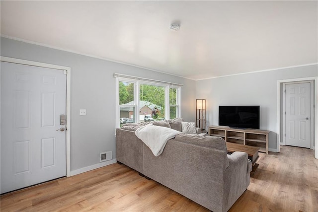 living room featuring baseboards, ornamental molding, light wood finished floors, and visible vents