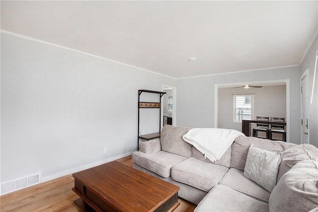 living room featuring baseboards, crown molding, visible vents, and wood finished floors