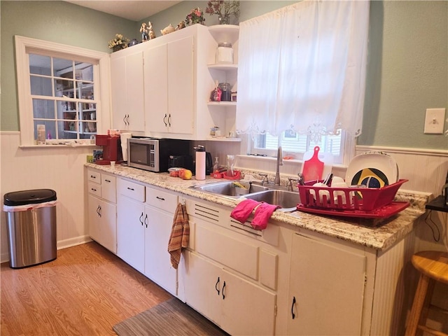 kitchen with open shelves, light wood-type flooring, light countertops, stainless steel microwave, and a sink