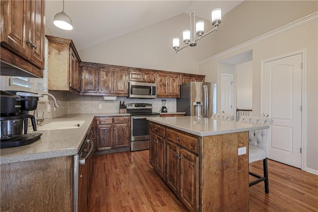 kitchen with appliances with stainless steel finishes, a sink, backsplash, dark wood-style flooring, and decorative light fixtures