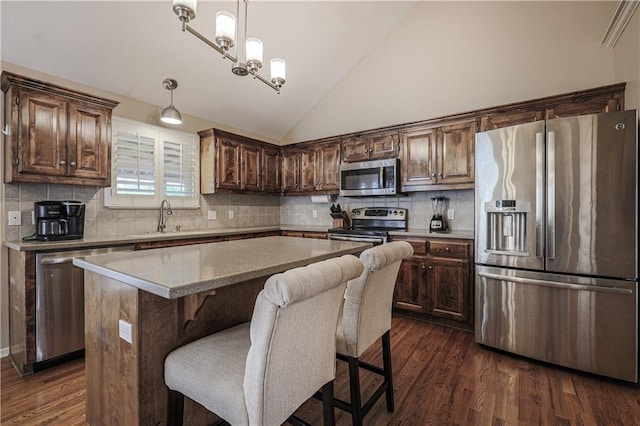 kitchen featuring stainless steel appliances, a kitchen island, lofted ceiling, dark wood finished floors, and decorative light fixtures