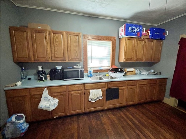kitchen with a sink, dark wood-type flooring, stainless steel microwave, light countertops, and ornamental molding