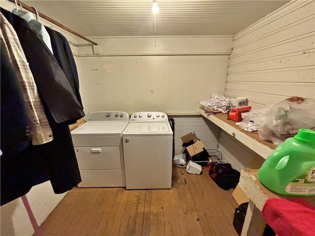 clothes washing area with light wood-style floors, wood walls, and washer and dryer