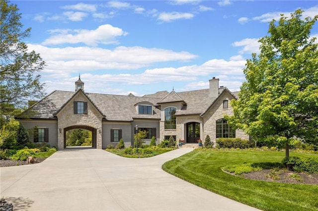 french country inspired facade featuring stone siding, a front yard, curved driveway, and a chimney