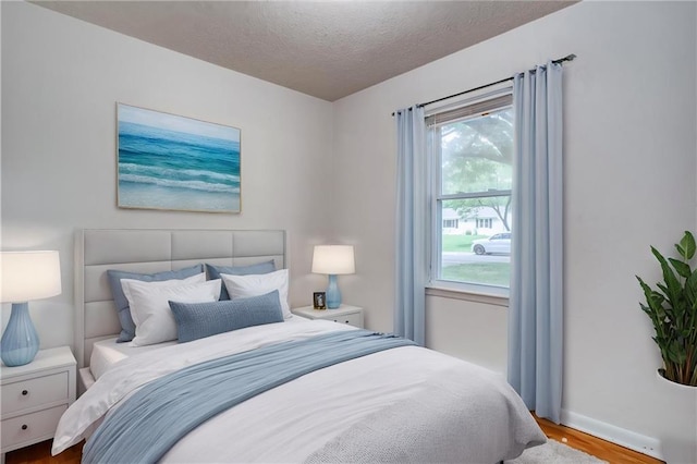 bedroom with wood finished floors, multiple windows, baseboards, and a textured ceiling