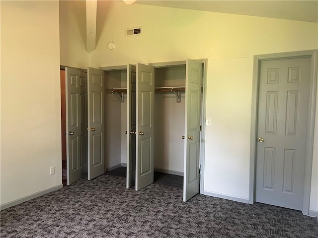 unfurnished bedroom with visible vents, beam ceiling, high vaulted ceiling, two closets, and dark carpet