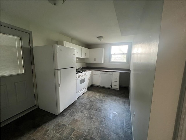 kitchen featuring dark countertops, stone finish floor, white appliances, and white cabinetry
