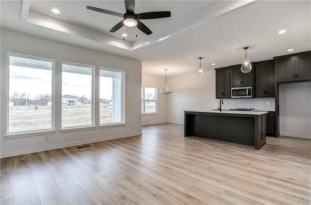16502 S Stagecoach St, Olathe, KS 66062 - kitchen with stainless steel microwave, a tray ceiling, ceiling fan, decorative backsplash, and light wood-type flooring