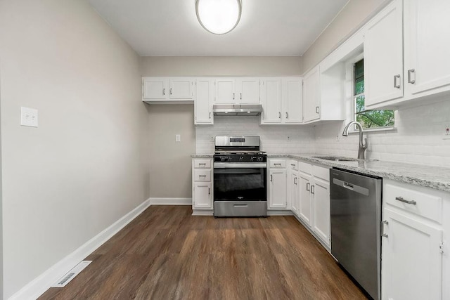kitchen with light stone countertops, a sink, stainless steel appliances, backsplash, and dark wood-style floors