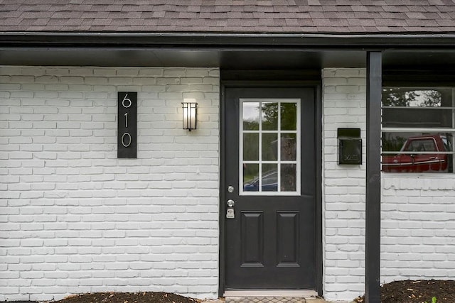 doorway to property featuring a shingled roof and brick siding