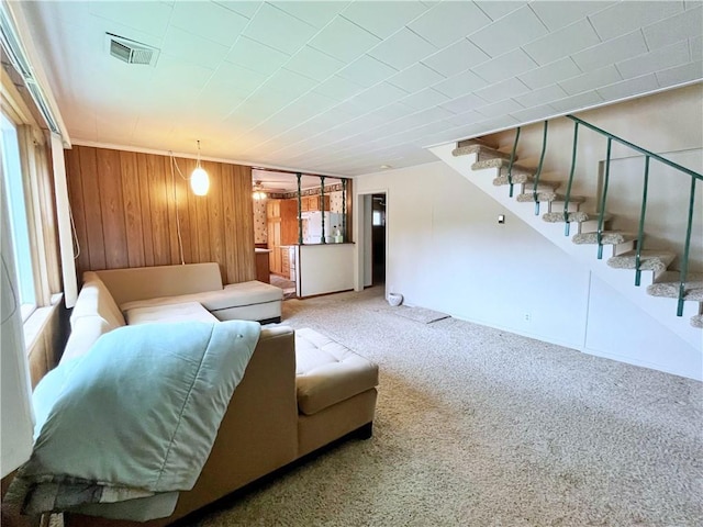 carpeted living area with wooden walls, visible vents, plenty of natural light, and stairway