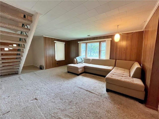 carpeted living room with stairway, crown molding, and wood walls
