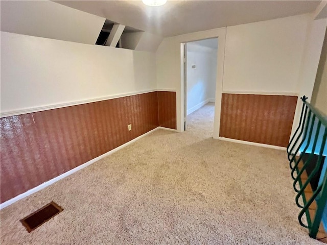 carpeted empty room featuring wooden walls, visible vents, lofted ceiling, and a wainscoted wall