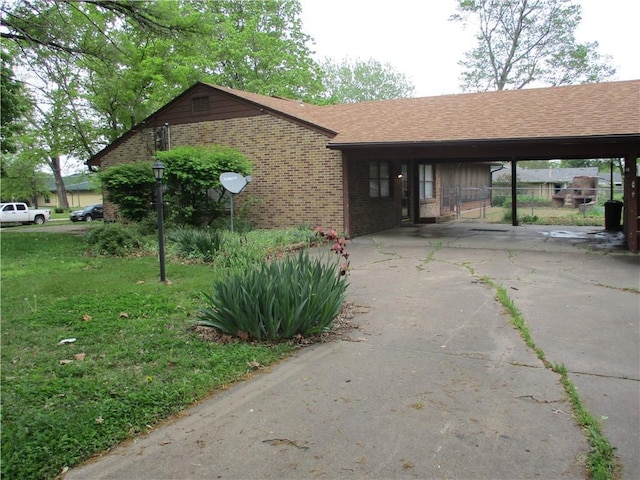 view of side of home with brick siding, a shingled roof, a lawn, driveway, and a carport
