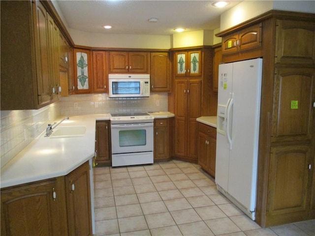 kitchen with a sink, tasteful backsplash, brown cabinetry, and white appliances