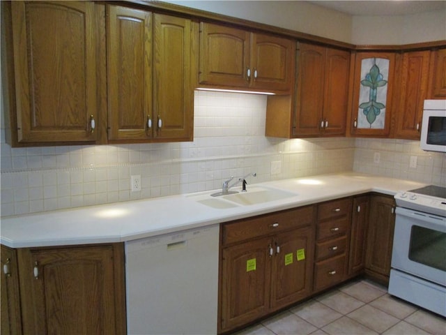 kitchen with a sink, decorative backsplash, brown cabinets, and white appliances