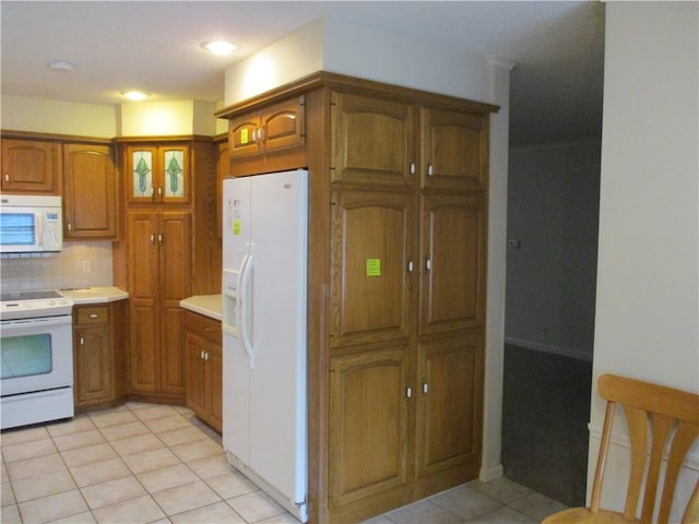 kitchen with brown cabinets, white appliances, light countertops, light tile patterned floors, and backsplash