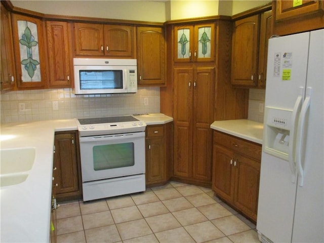 kitchen with white appliances, light countertops, brown cabinetry, backsplash, and glass insert cabinets