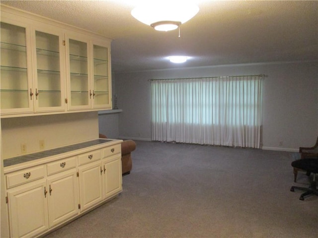 interior space with carpet floors, open floor plan, baseboards, and glass insert cabinets