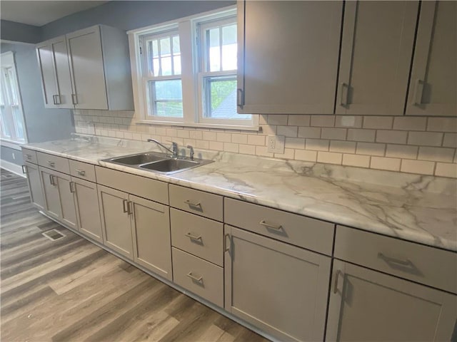 kitchen featuring baseboards, gray cabinets, a sink, light wood finished floors, and backsplash