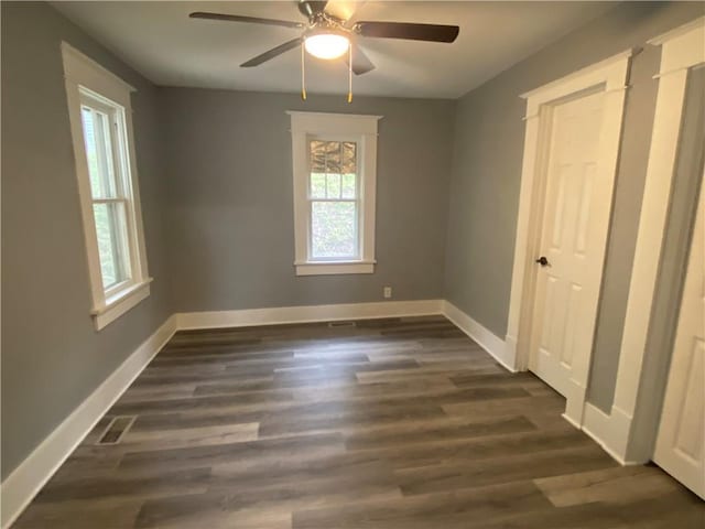 unfurnished room with baseboards, a ceiling fan, dark wood-style floors, and visible vents