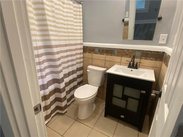 full bath with vanity, toilet, tile patterned floors, a wainscoted wall, and tile walls