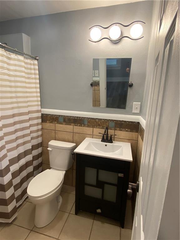 full bath with toilet, tile walls, tile patterned flooring, and a wainscoted wall