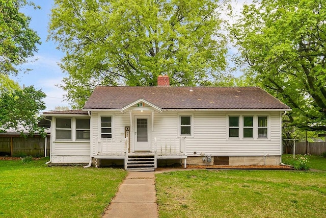 view of front of house featuring fence, a chimney, roof with shingles, and a front lawn