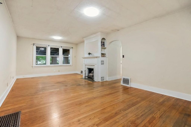 unfurnished living room featuring arched walkways, light wood-style flooring, and visible vents