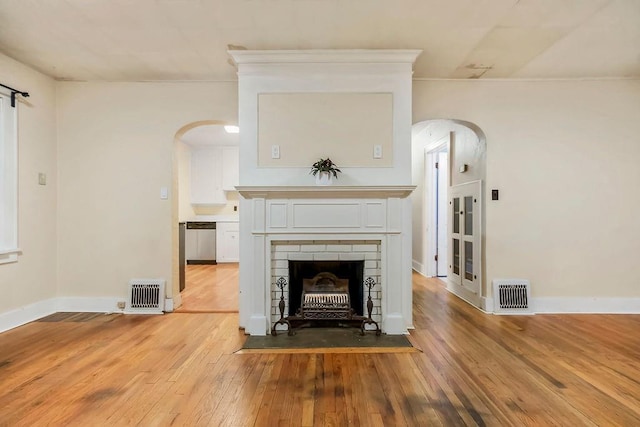 unfurnished living room with a brick fireplace, arched walkways, visible vents, and wood finished floors