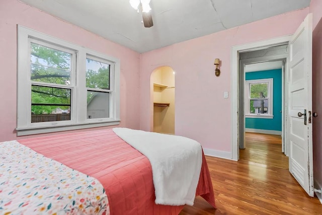bedroom with baseboards, multiple windows, a ceiling fan, and wood finished floors