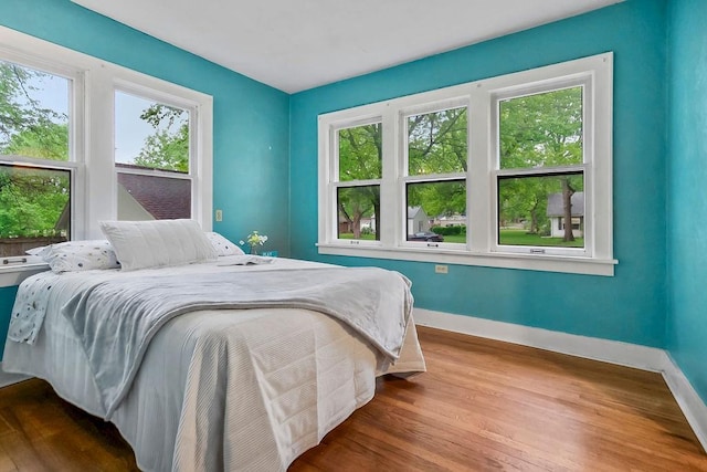 bedroom with baseboards, wood finished floors, and multiple windows