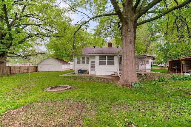 rear view of property featuring fence, a chimney, a lawn, and an outdoor fire pit