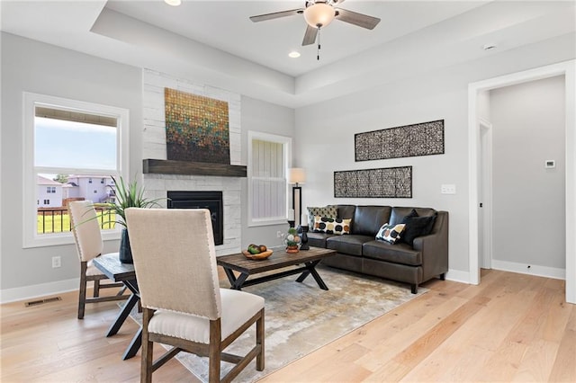 living room featuring ceiling fan, visible vents, a large fireplace, baseboards, and light wood-style flooring