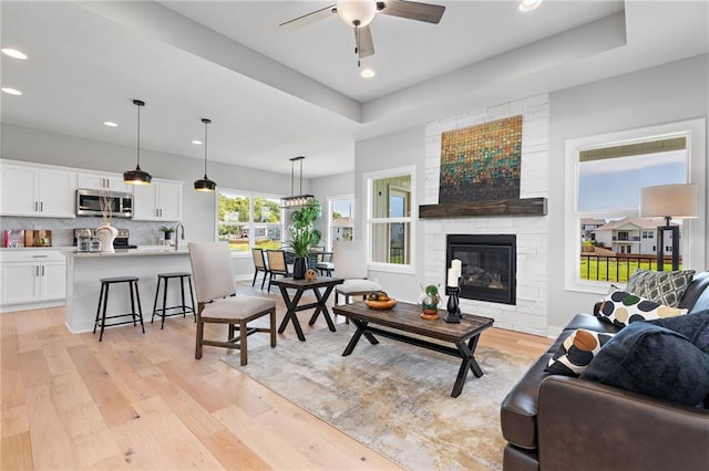 living room with ceiling fan, a raised ceiling, a fireplace, recessed lighting, and light wood-type flooring